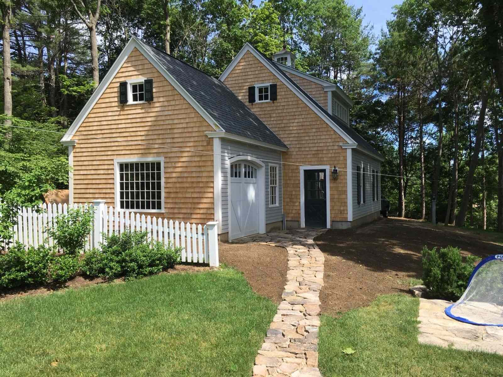Garage with cedar shake siding and a white picket fence, designed by Oxland Builders in New Hampshire Garage with cedar shake siding and a white picket fence, designed by Oxland Builders in New Hampshire