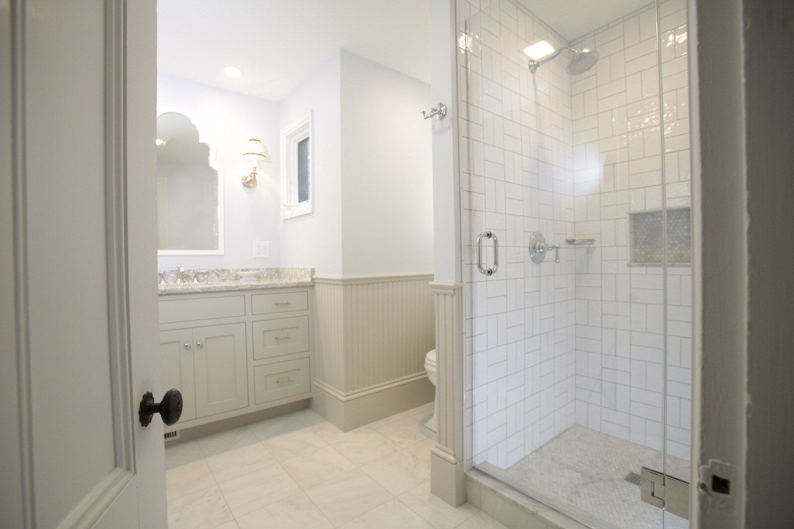 Minimalist white-tiled shower with glass doors and built-in shelving, designed by Oxland Builders in New Hampshire
