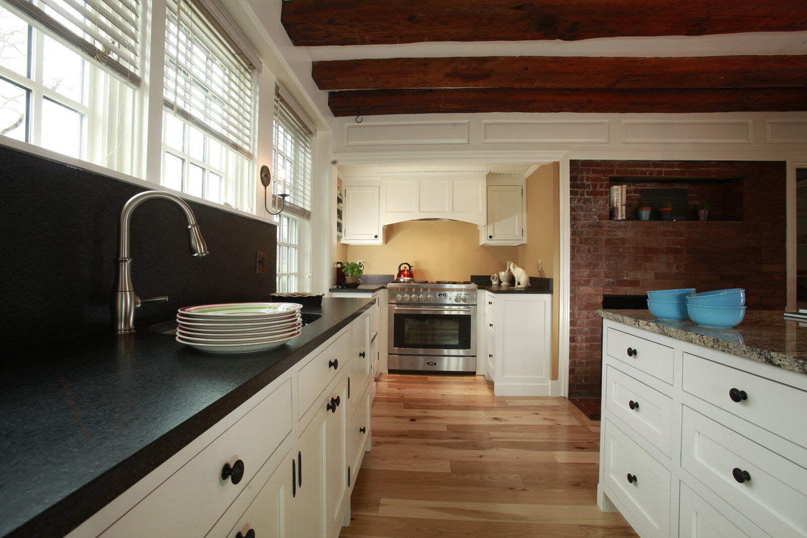 Rustic farmhouse kitchen with exposed wooden beams and white cabinetry, designed by Oxland Builders in New Hampshire