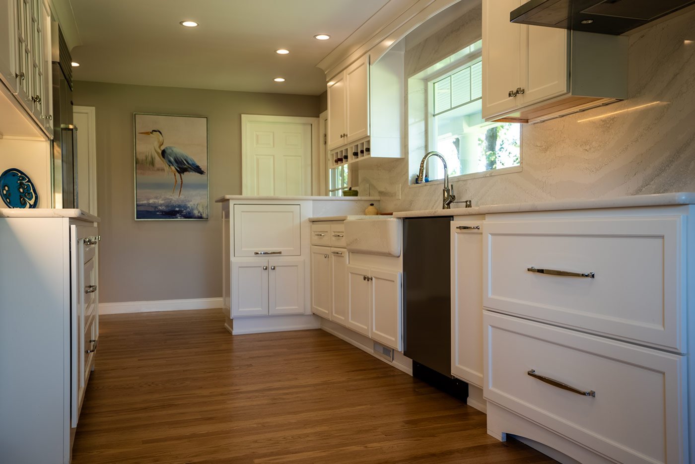 Bright New Hampshire kitchen with white cabinetry, marble backsplash, and a farmhouse sink below a wide window