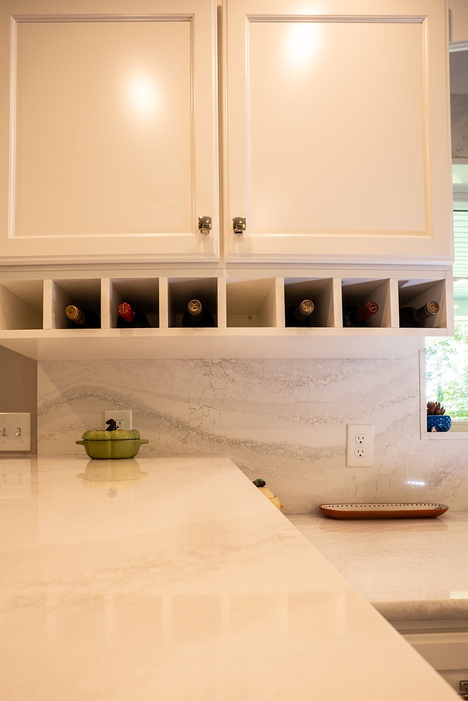 Built-in wine storage below white cabinets in a marble-accented kitchen by Oxland Builders in New Hampshire