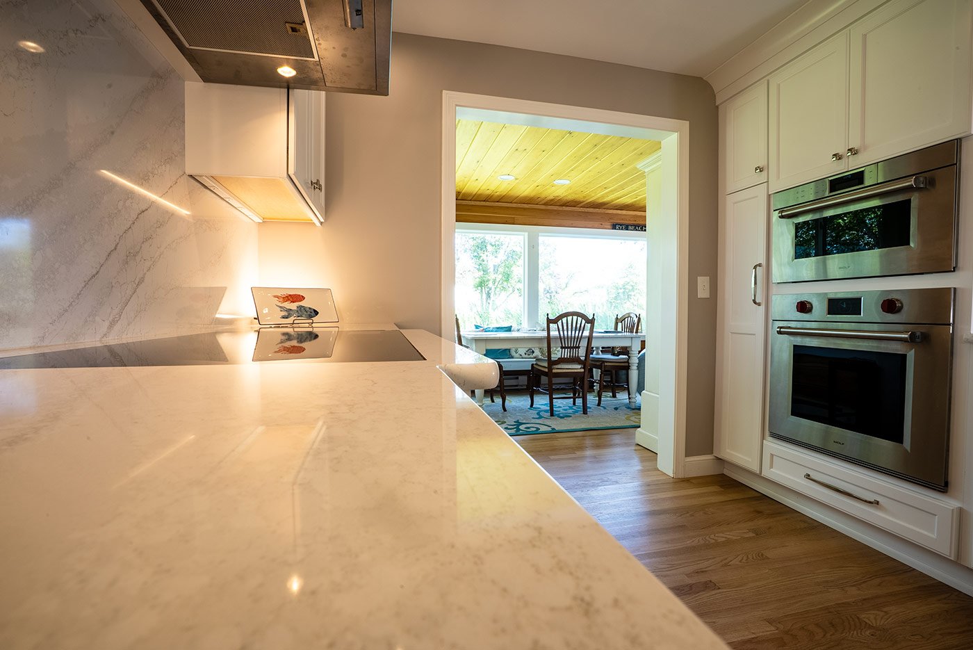 Clean marble counters and white cabinetry in a New Hampshire kitchen, leading into a cozy dining nook with natural light