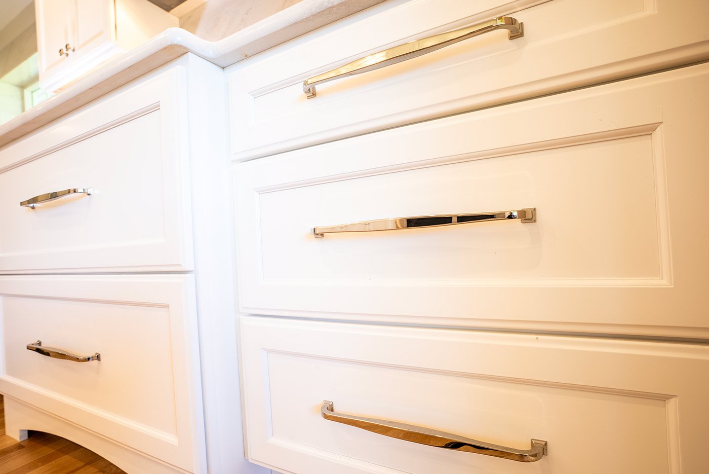 Close-up of elegant white kitchen drawers with sleek chrome handles in a coastal New Hampshire home, highlighting refined cabinetry craftsmanship