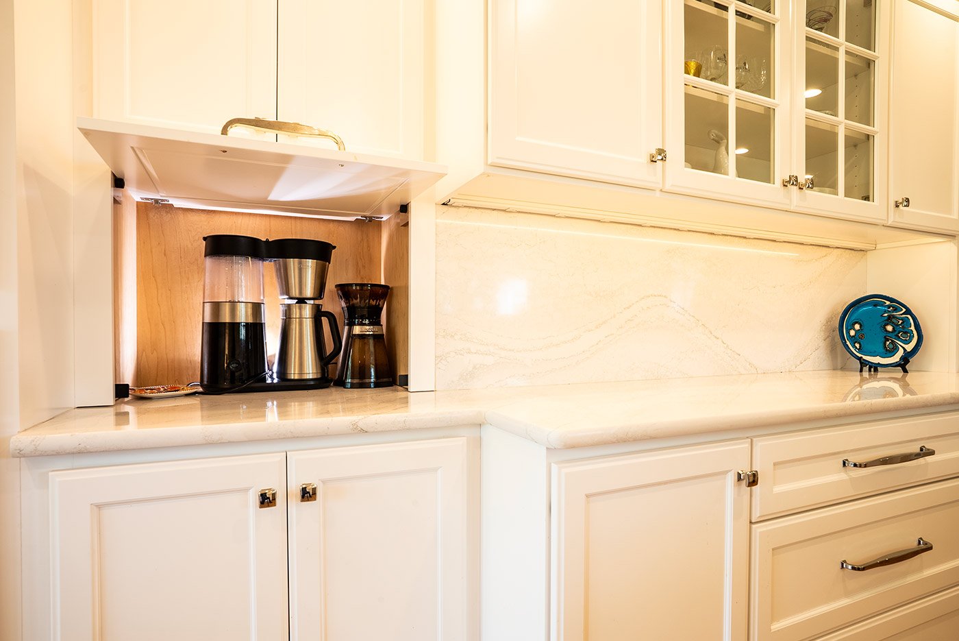 Coffee bar with stainless steel brewers and warm under-cabinet lighting in a Seacoast, NH kitchen by Oxland Builders
