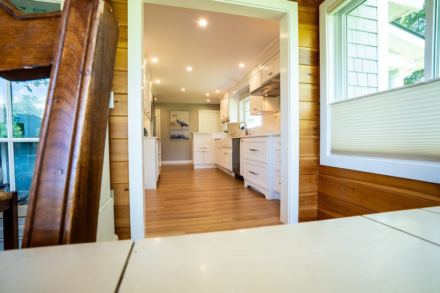 New Hampshire sunroom entrance opening into white Oxland Builders kitchen with recessed lighting