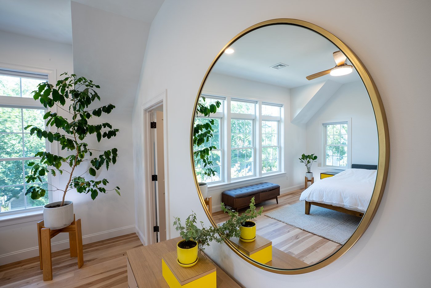 Coastal New Hampshire bedroom reflected in a round mirror above a dresser with potted plants and bright yellow accents Coastal New Hampshire bedroom reflected in a round mirror above a dresser with potted plants and bright yellow accents
