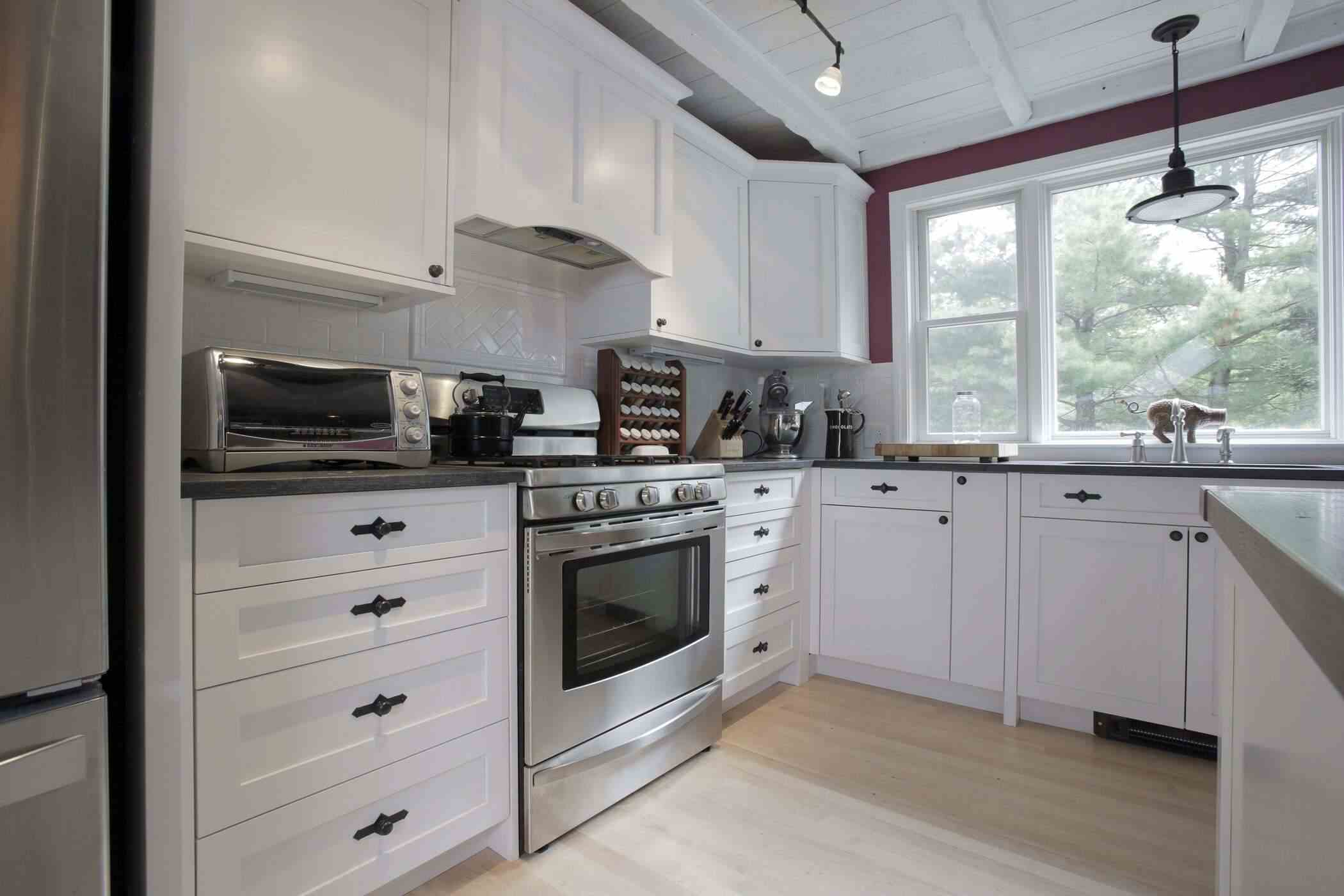 Bright Coastal NH kitchen with white cabinetry, stainless steel appliances, large window, and light wood flooring