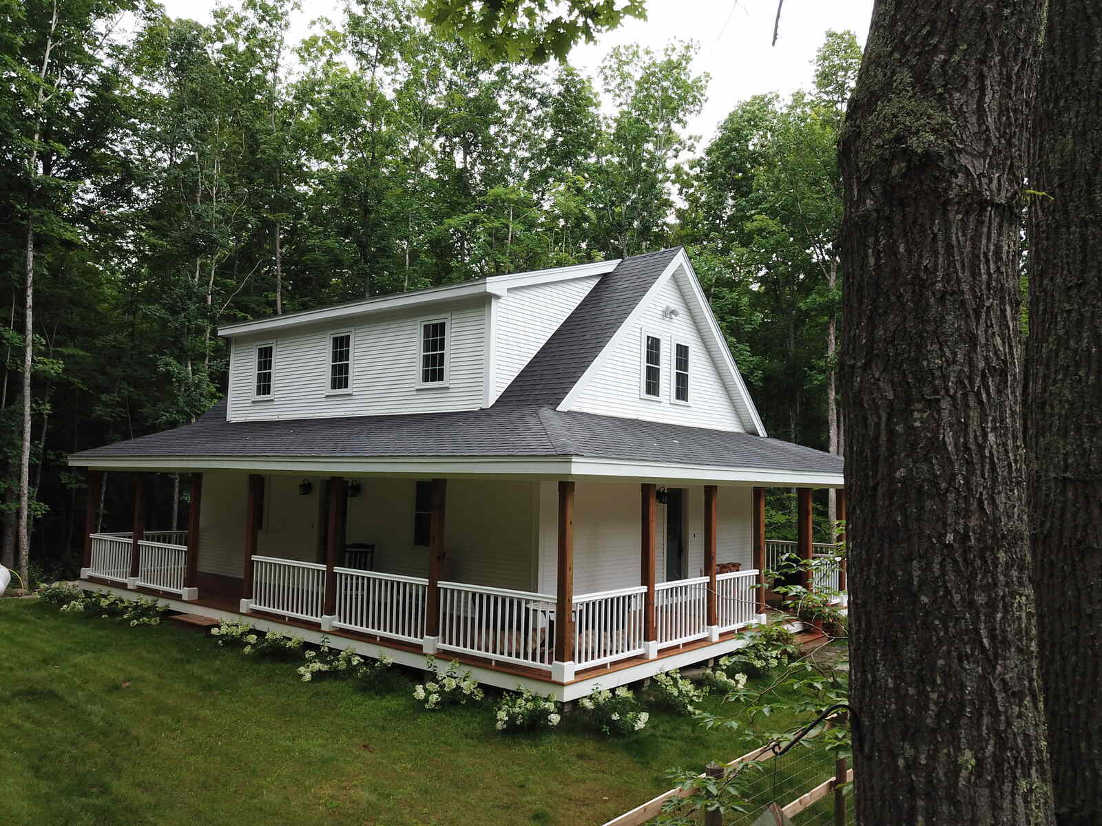 Aerial view of a custom home with a wraparound porch, surrounded by forested landscape, built by Oxland Builders in New Hampshire