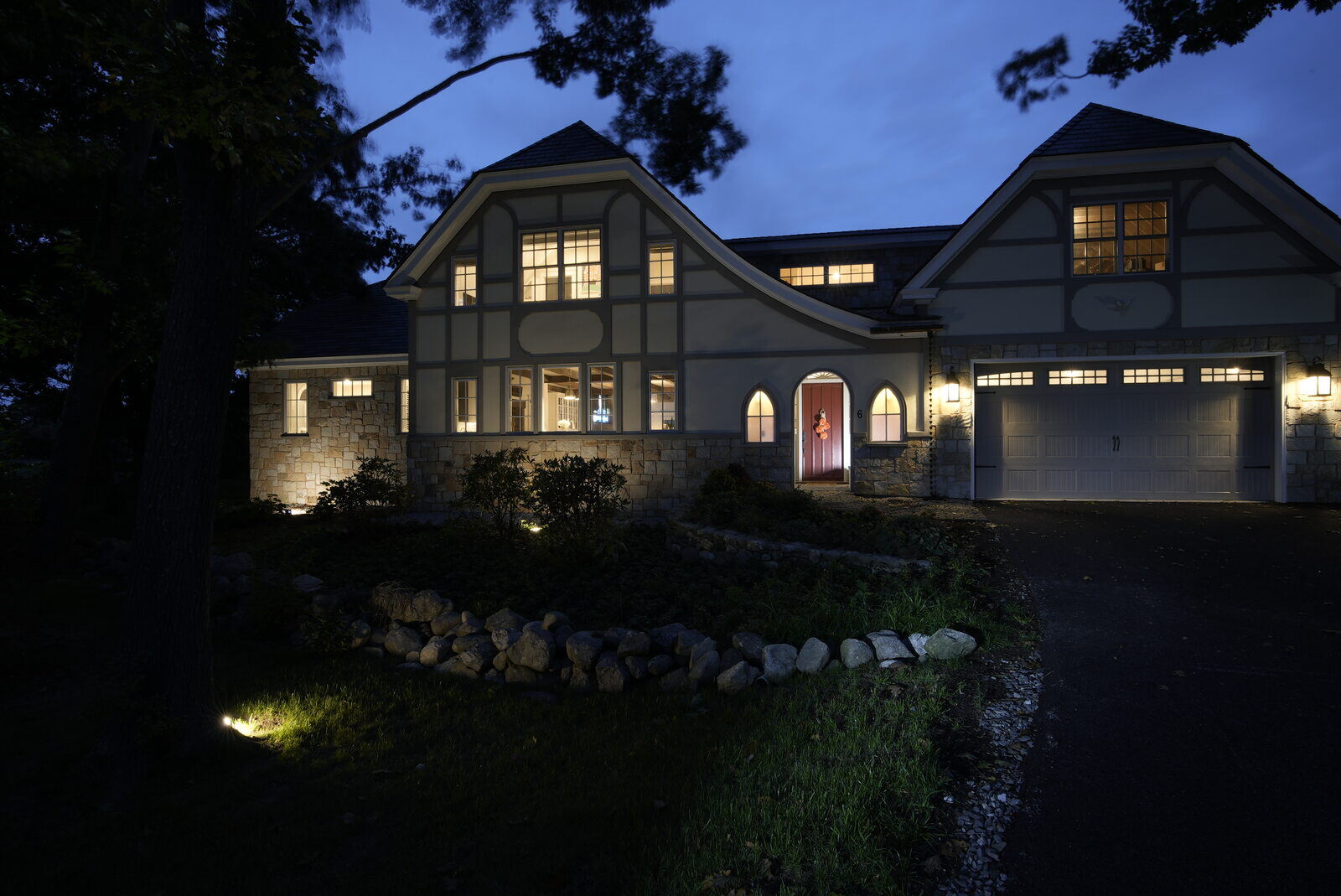 Tudor-style home illuminated at night, showcasing elegant stonework and custom lighting by Oxland Builders in New Hampshire