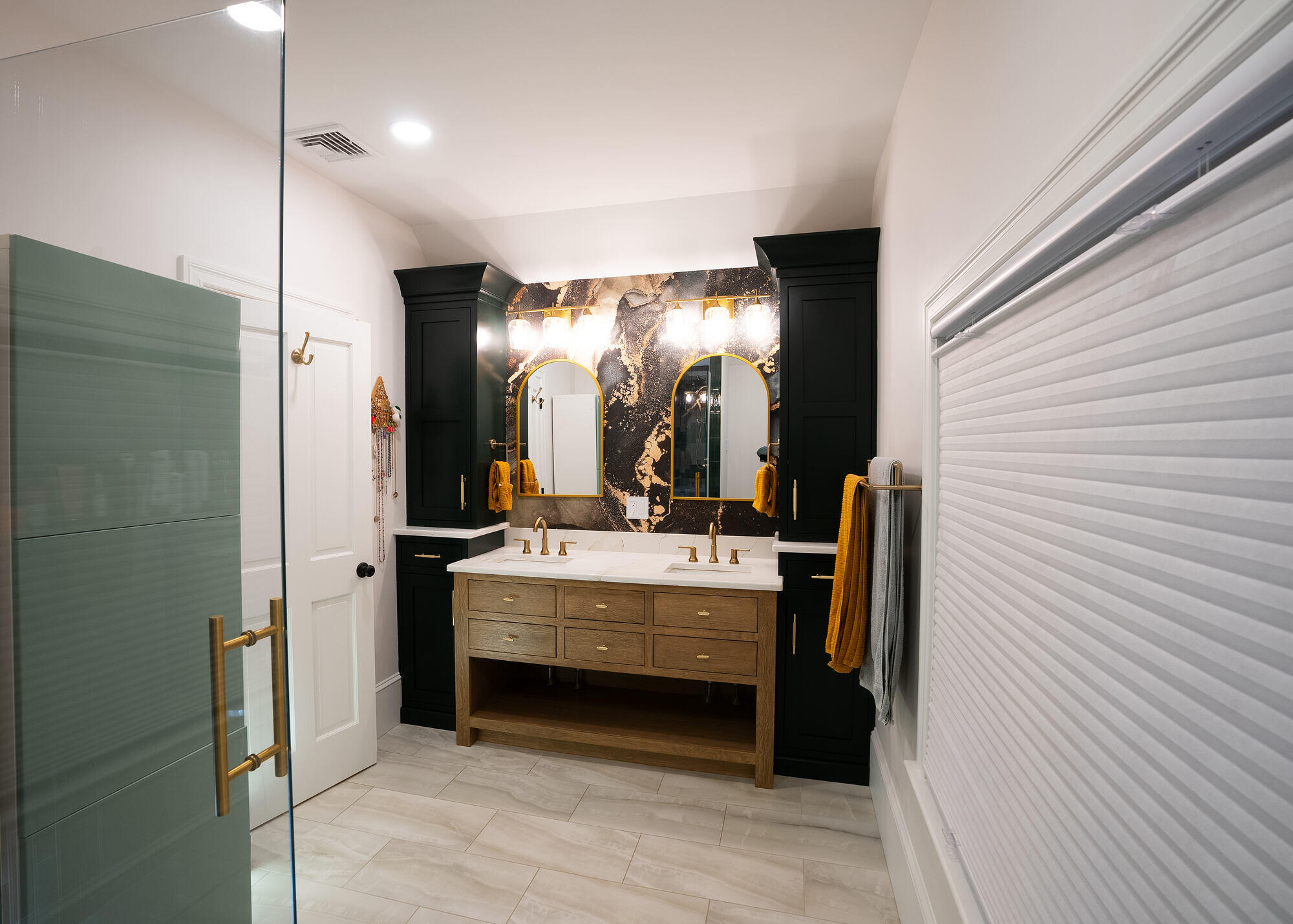 Modern bathroom renovation featuring dual sinks, gold fixtures, and bold marble wall accents by Oxland Builders in New Hampshire