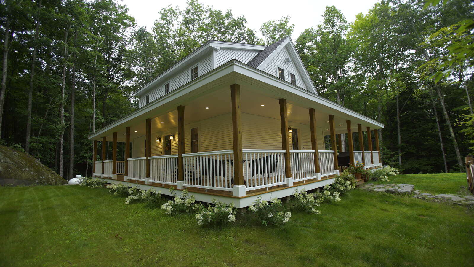 Custom-built home with a wraparound porch surrounded by greenery in New Hampshire, designed by Oxland Builders