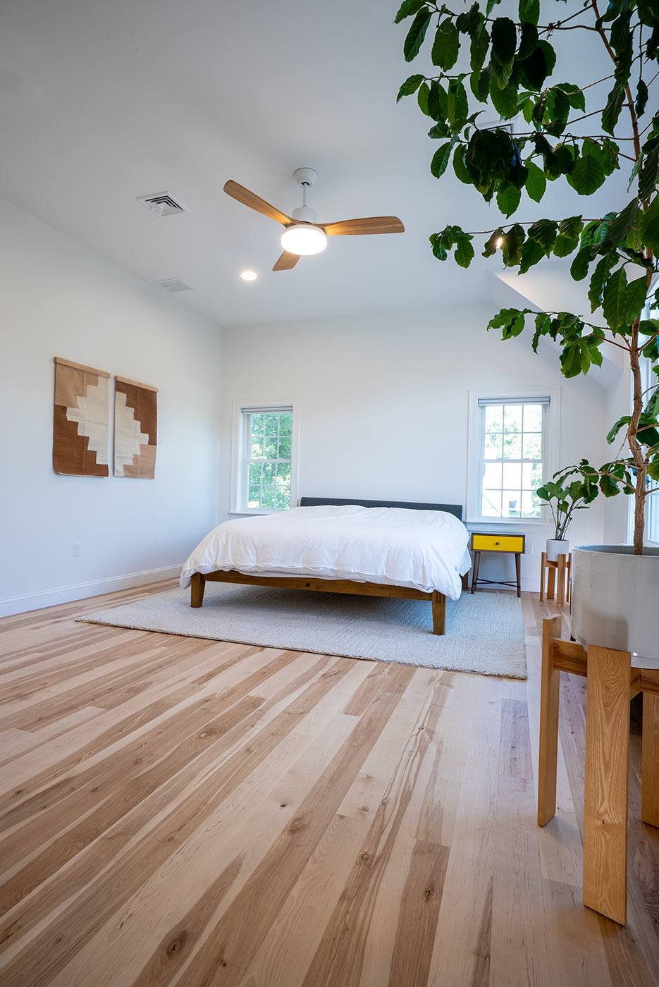 Coastal New Hampshire bedroom featuring a platform bed, white bedding, natural light, and vibrant green indoor plant in the foreground