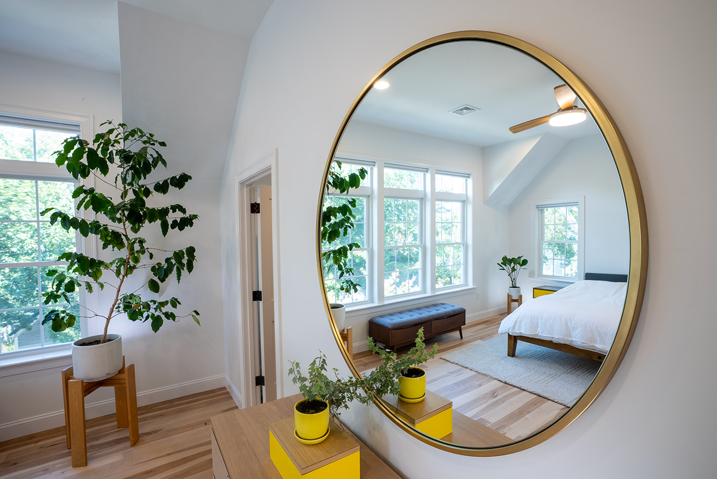 Coastal New Hampshire bedroom reflected in a round mirror above a dresser with potted plants and bright yellow accents